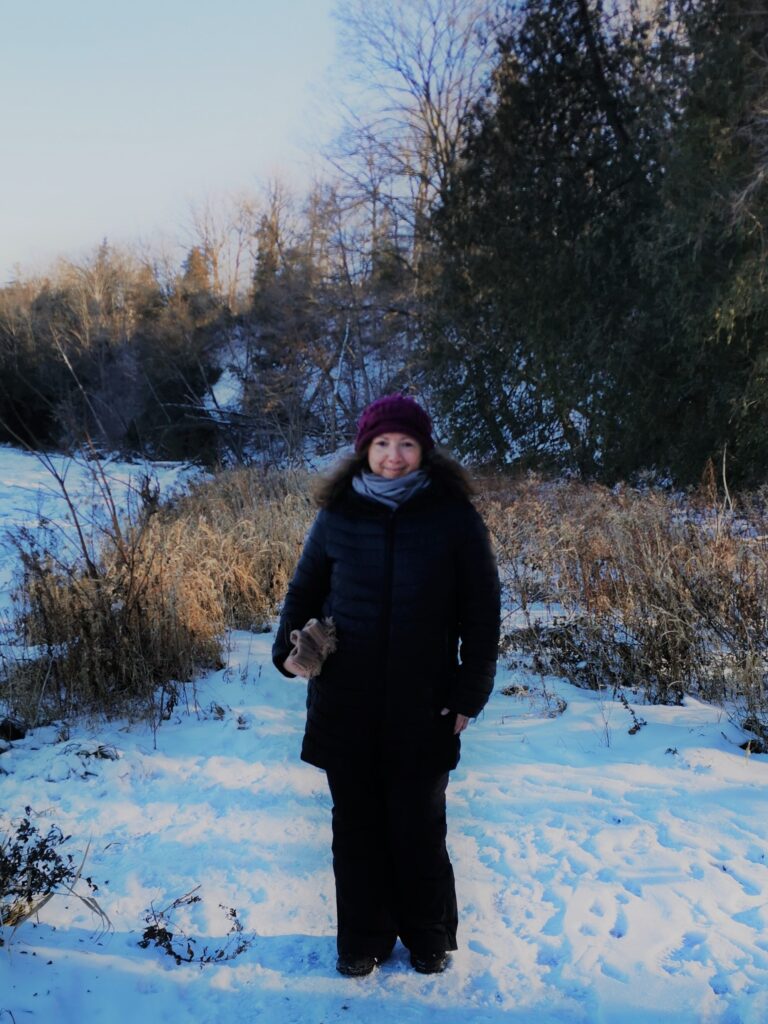 Mariam Pirbhai, author of Outside People and Other Stories (2017) and Isolated Incident (2022) bundled up in toque and parka on the snow-covered bank of the Grand River near Waterloo, Ontario.